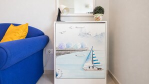 Una habitación con un sofá azul, un armario blanco con un cuadro de un velero, y una pequeña planta en maceta encima.