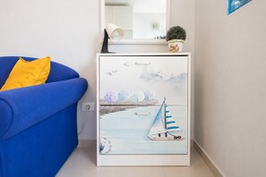 A room with a blue sofa, a white cabinet with a painting of a sailboat, and a small potted plant on top.