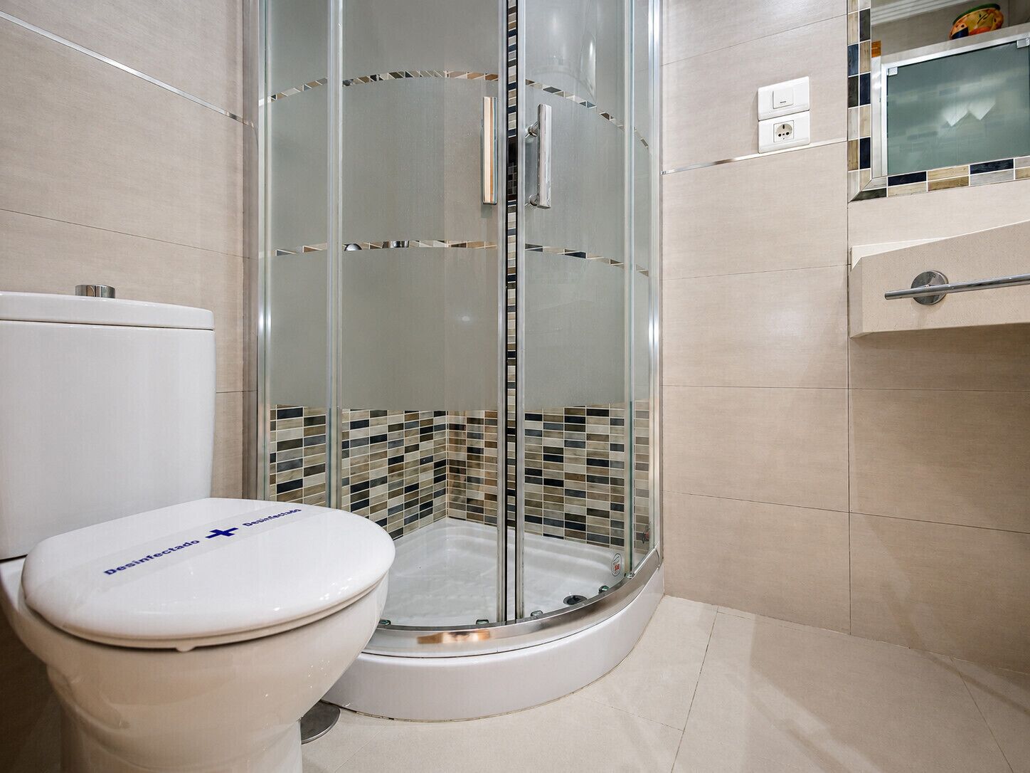Ein Badezimmer mit Toilette, einer gläsernen Duschkabine und einer gefliesten Wand.