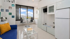 A modern living room with a blue sofa, a glass coffee table, and a dining area with two chairs. - Sun Port Ocean Views - Renovated & Pool 1 (Puerto Rico)