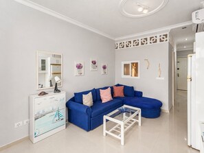 A living room with a blue sofa, a glass coffee table, and a white cabinet with artwork. - Sun Port Ocean Views - Renovated & Pool 1 (Puerto Rico)