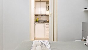 A bedroom with a bed, a bedside table, and a view into a kitchen with cabinets and a microwave. - Sun Port Ocean Views - Renovated & Pool 1 (Puerto Rico)
