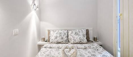 A hotel room with a bed, a nightstand, a wall-mounted light fixture, and a door.