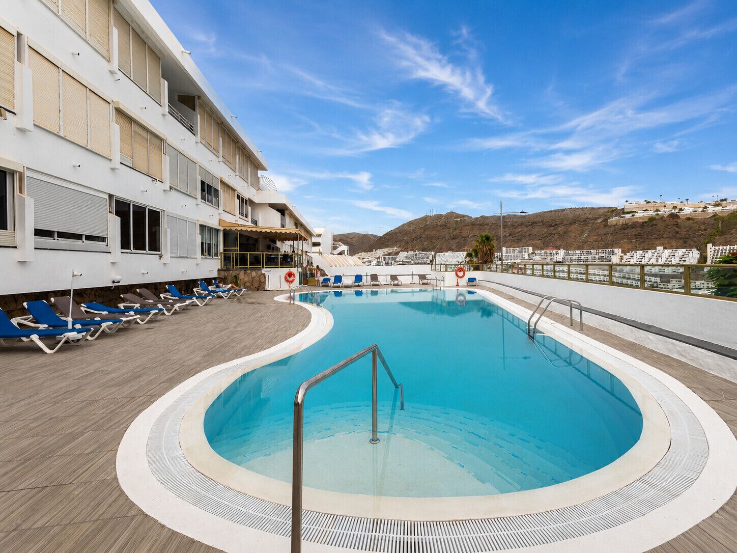A swimming pool with lounge chairs and a building with balconies.