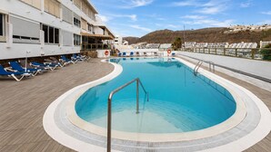 A swimming pool with lounge chairs and a building with balconies. - Sun Port Ocean Views - Renovated & Pool 1 (Puerto Rico)
