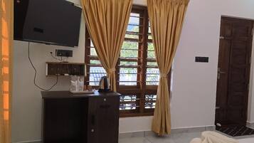 Habitación de hotel con cama, televisión, escritorio y ventana con cortinas.