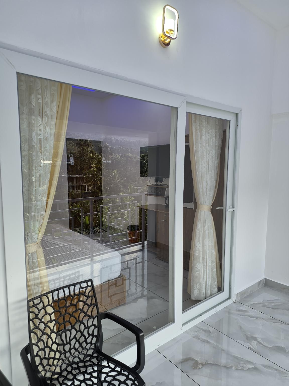 Un interior moderno con un vidrio corredizo que da a un espacio exterior, un sillón estampado y una lámpara fijada a la pared.