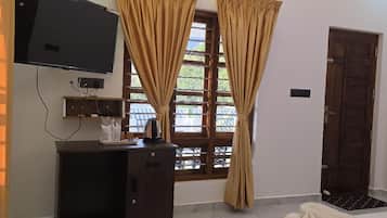 Quarto de hotel com cama, secretária e televisão, e cortinas.