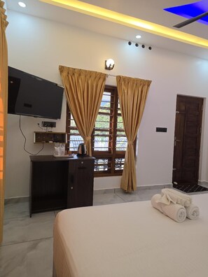 A hotel room with a bed, a desk with a television, and curtains. - Rosa Mystica Hotels & Resorts (Devikolam)