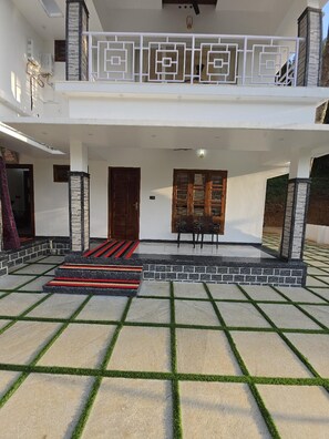 A two-story building with a balcony, a wooden door, and a seating area with chairs. - Rosa Mystica Hotels & Resorts (Devikolam)