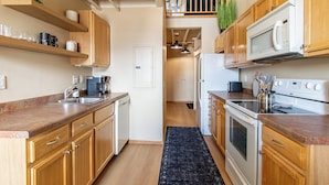 A compact kitchen with wooden cabinets, a microwave, a stove, and a coffee maker.