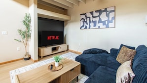 A living room with a television displaying 'NETFLIX', a sofa, a coffee table, and a plant.