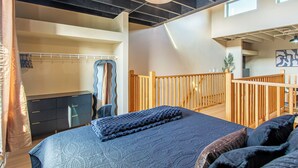 A bedroom with a large bed, a wooden railing, a wardrobe, and a mirror.