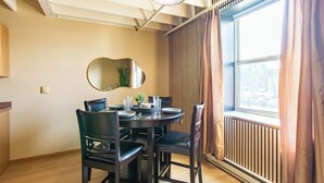 A dining area with a round table, four chairs, a mirror, and a window with curtains.