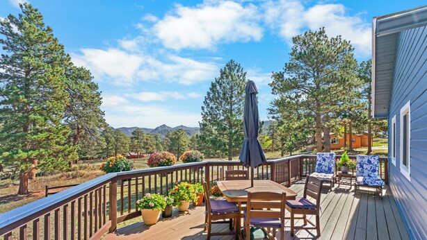 A wooden deck with outdoor furniture, potted plants, and a view of mountains. - Whispering Pines Getaway with hot tub, large deck, game room and wildlife views (Estes Park)