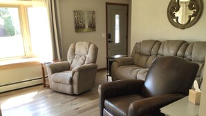 Un salon avec deux fauteuils en cuir, une petite table d’appoint blanche et un tableau accroché au mur.