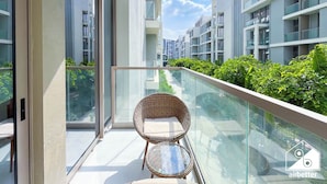 Varanda com cadeira de vime e uma pequena mesa, com vista para uma fileira de edifícios residenciais modernos e vegetação exuberante.