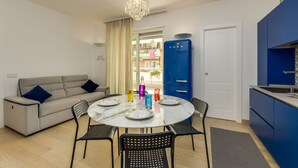 Een moderne woonkamer met een ronde eettafel, een bank en een keuken met blauwe kastjes.