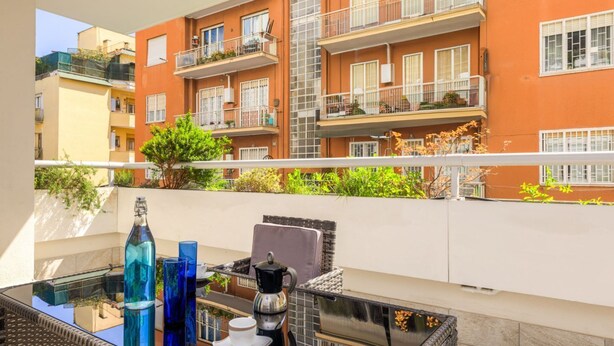 Een balkon met een glazen tafel, blauwe glazen flessen, een koffiepot en een witte beker.