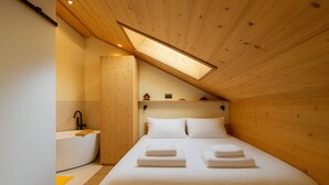 Un dormitorio con techo de madera, tragaluces, cama con ropa blanca y mesita de noche de madera.