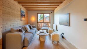 Una sala de estar acogedora con techo de madera, un conjunto de sofá, una mesa redonda de centro y un ventanal con vista a un edificio.