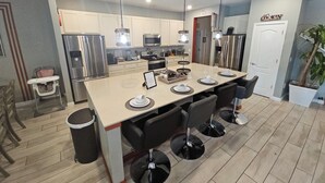 Une cuisine moderne dotée d’un îlot central, d’appareils électroménagers en acier inoxydable et d’un coin repas avec des tabourets de bar.