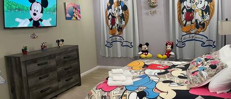 A bedroom with Mickey and Minnie Mouse themed decor, including curtains, bedding, and wall art.