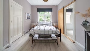 Una camera da letto con una struttura del letto in metallo, una finestra che si affaccia sul verde, una porta bianca e uno specchio appeso al muro.