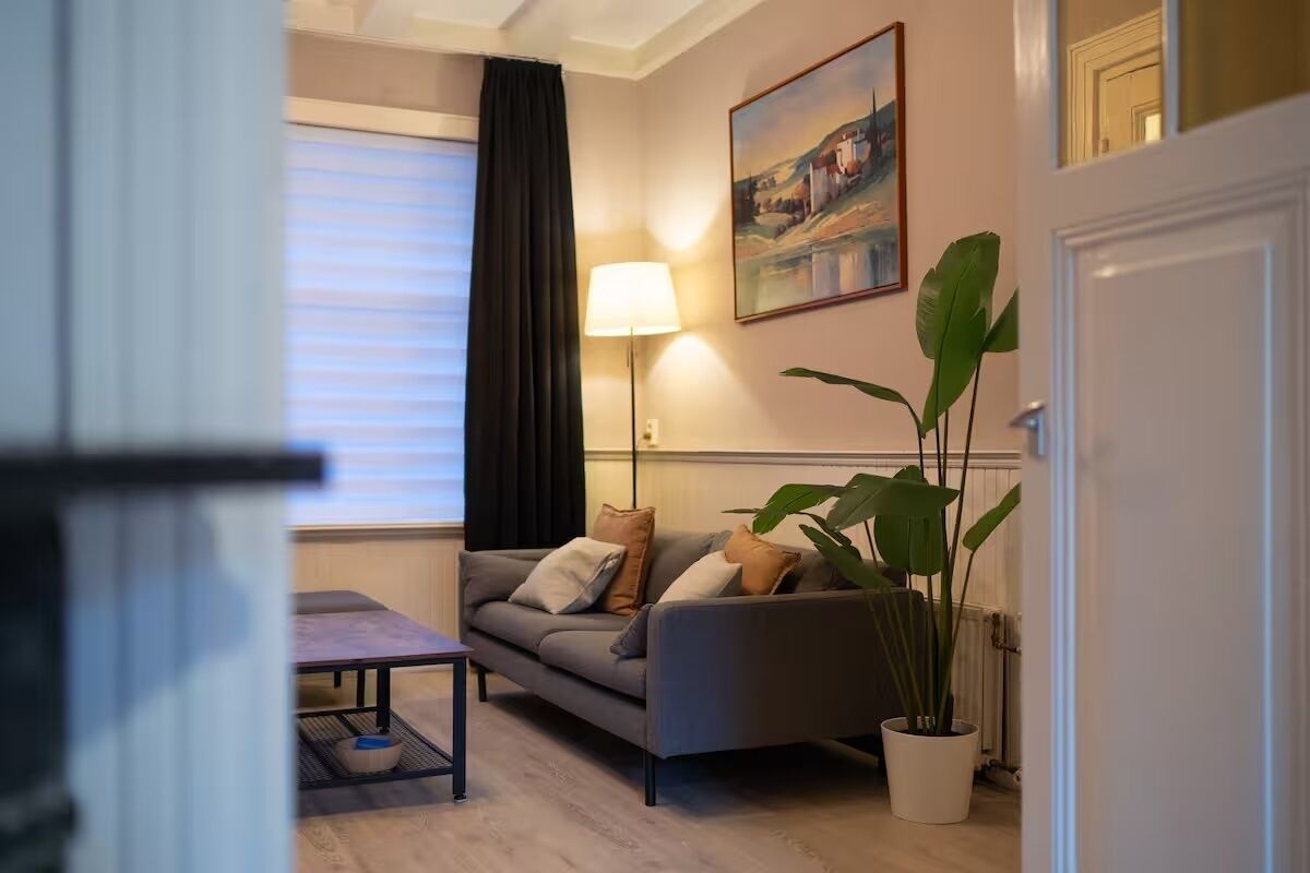 A living room with a sofa, a table, a lamp, and a potted plant.
