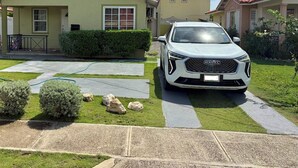 Une maison à deux étages avec un toit recouvert de tuiles rouges, une allée et une voiture blanche garée devant.