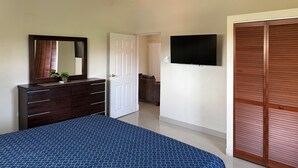 Une chambre à coucher comprenant un lit, une commode, un miroir, un ventilateur de plafond, une télévision et une armoire.