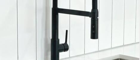 Cozinha moderna com torneira preta, azulejos brancos e uma pia retangular.