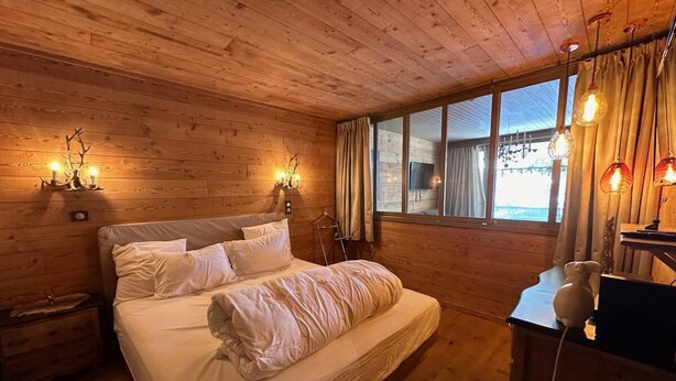 Et hyggeligt soveværelse i en træhytte med seng, sengeborde og et skrivebord med lampe.