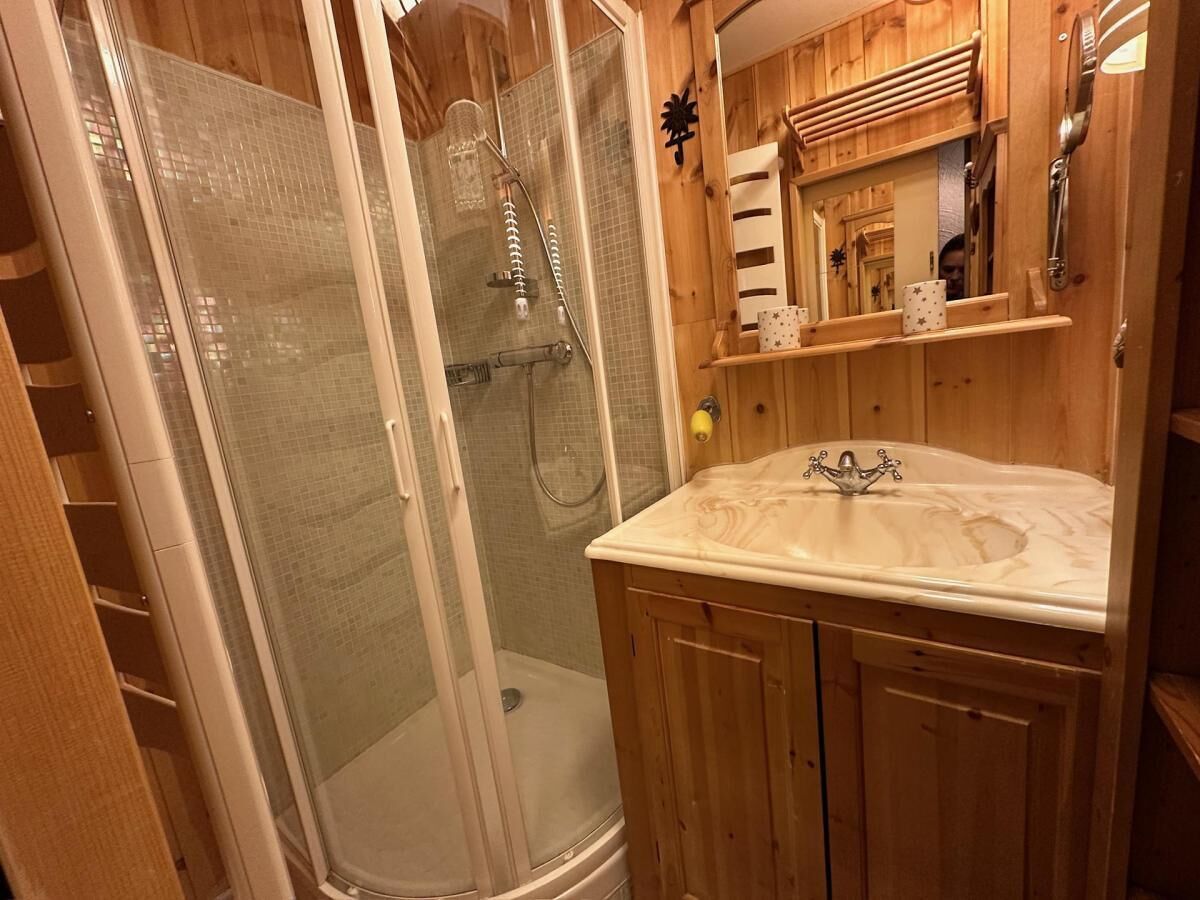 Een houten badkamer met een douche met glazen wand, een wastafel met een marmeren blad en een spiegel boven de wastafel.