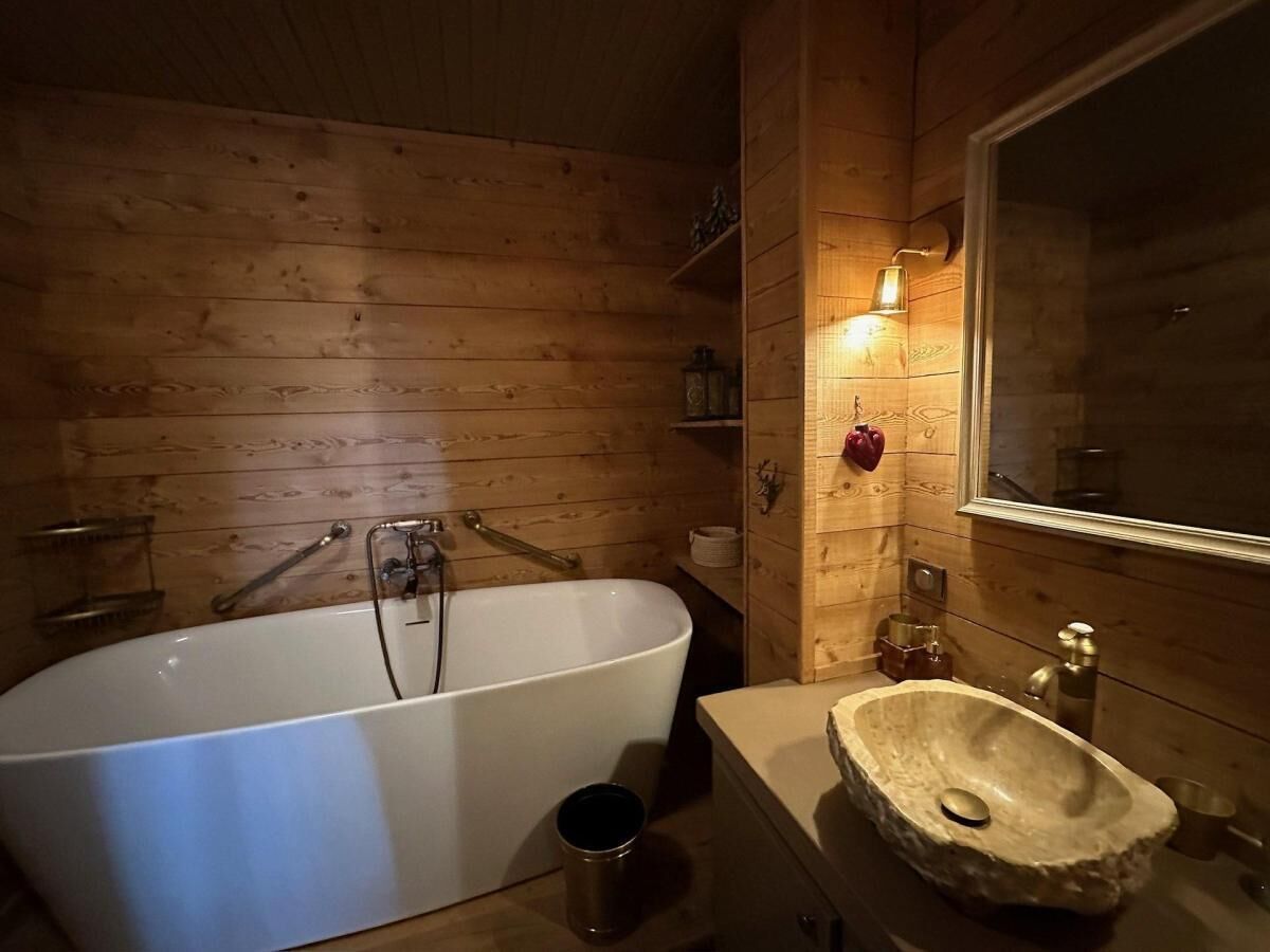 A wooden cabin bathroom with a freestanding bathtub, a stone sink, and a mirror.