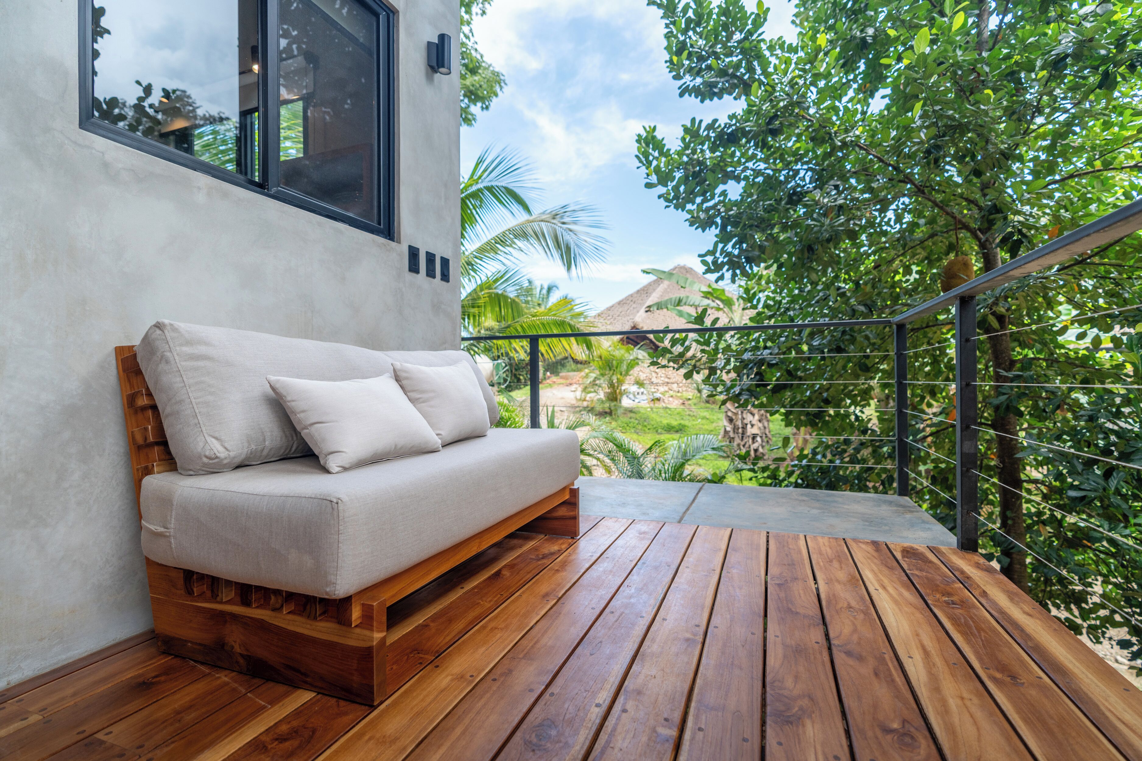 A wooden deck with a sofa and a railing overlooking a garden.