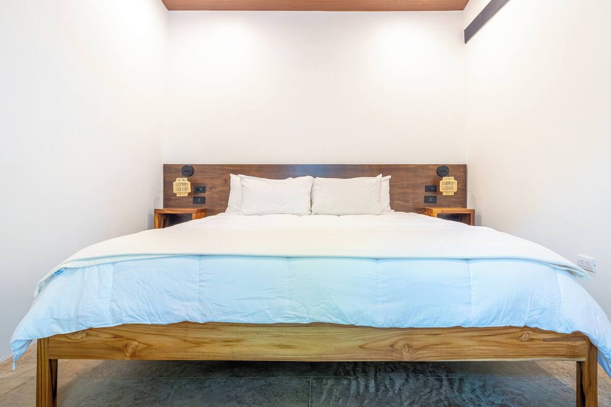 Una cama bien hecha con cabecera de madera, ropa de cama blanca y dos mesitas de noche con lámparas.