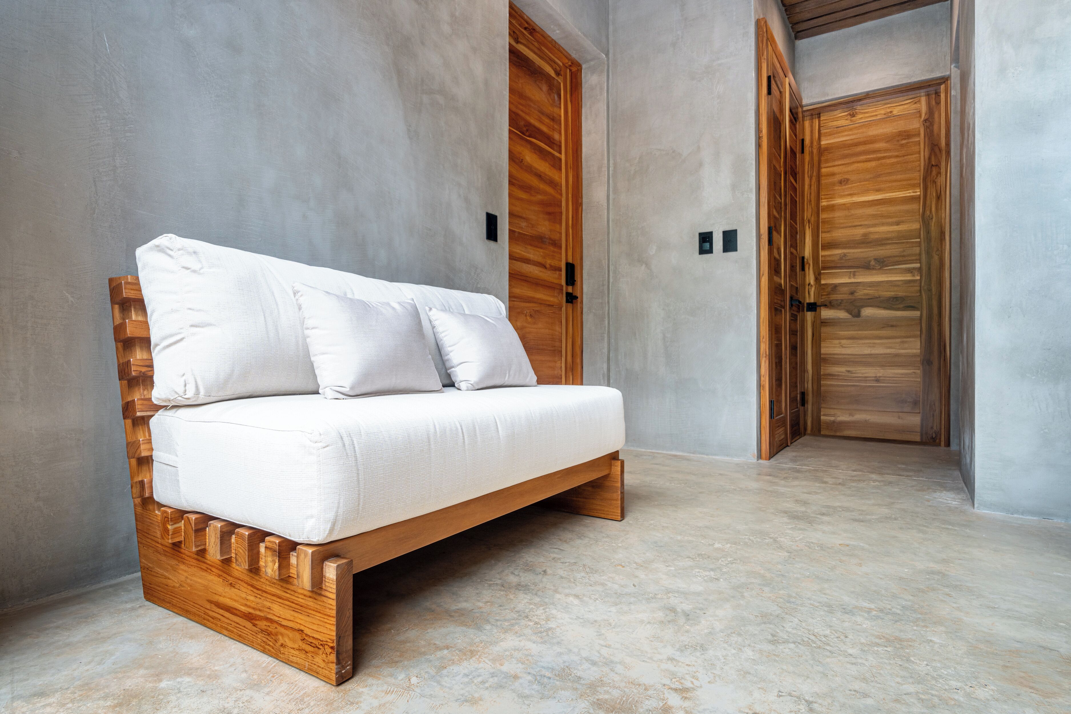 A modern room with a wooden sofa, a large wooden door, and a concrete floor.