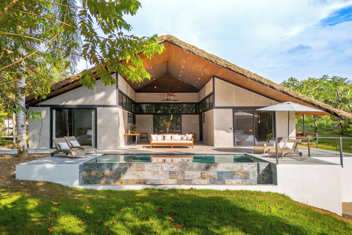 Una casa moderna con un amplio frente de vidrio, piscina y zonas de estar exteriores.