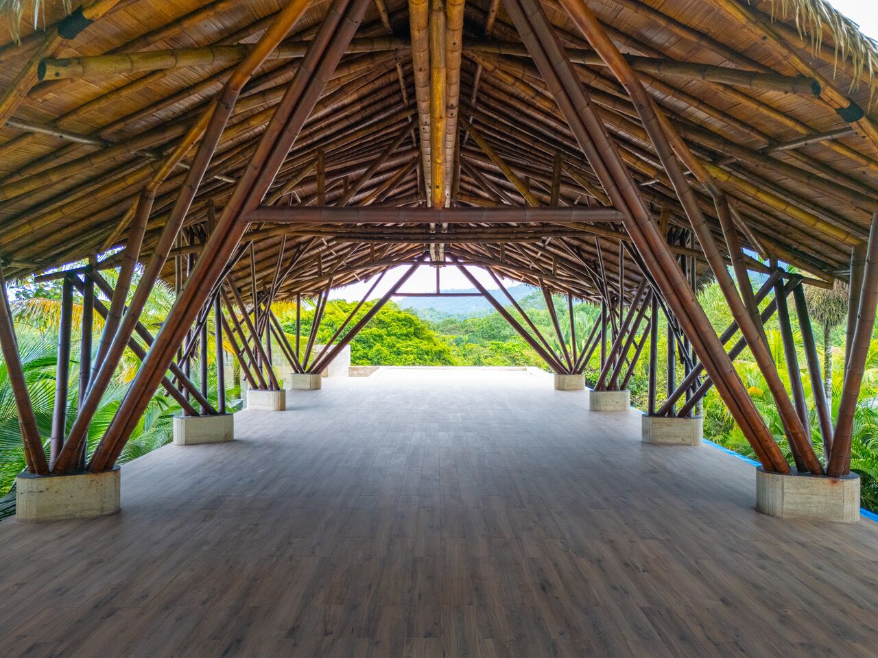 Eine offene Pagode mit Holzboden und einem Reetdach, gestützt von Bambuspfählen.