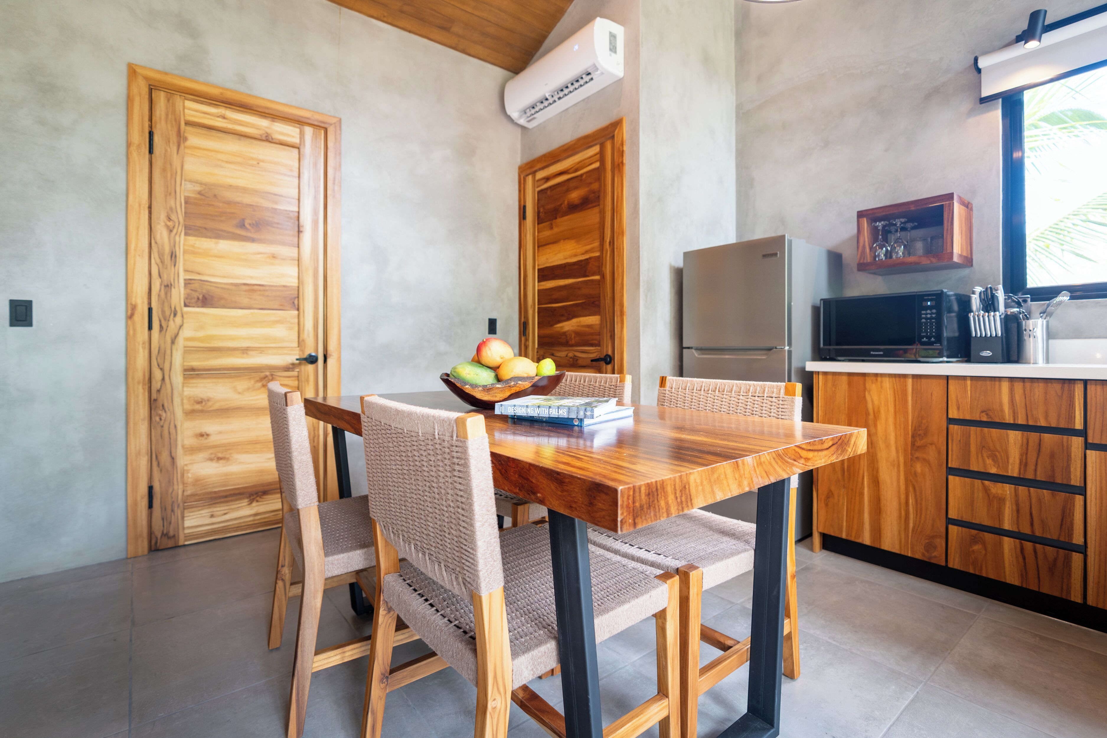 A dining area with a wooden table and chairs, a fruit bowl, and a microwave in the background.