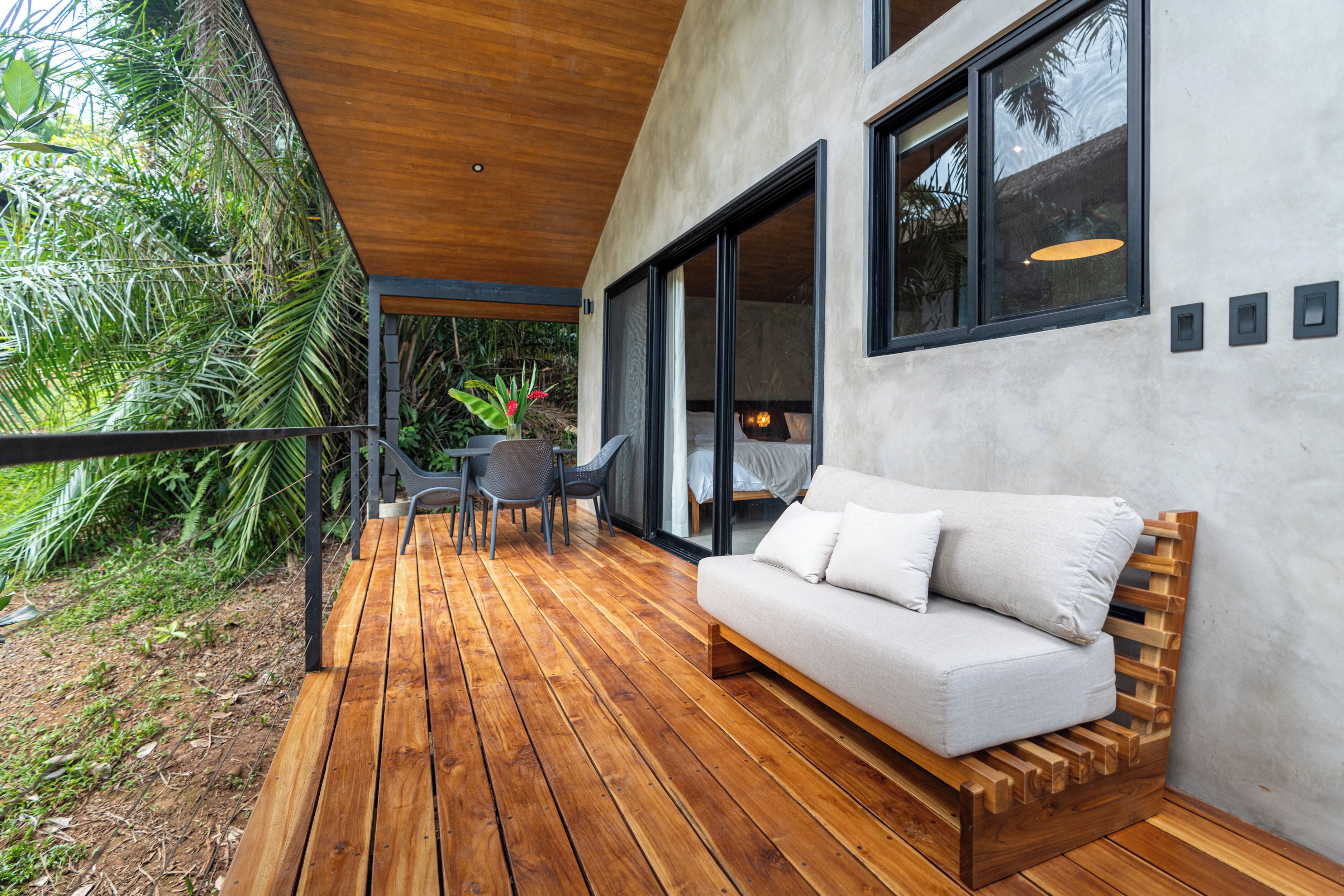 A wooden deck with a sofa and chairs, surrounded by lush greenery.