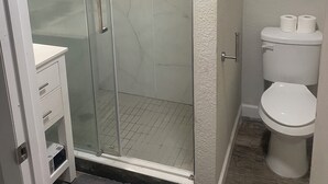 A bathroom with a glass-enclosed shower, a white toilet, and a vanity with drawers. - Cute 5-bedroom,6bed house in superb Winter Park. (Winter Park)