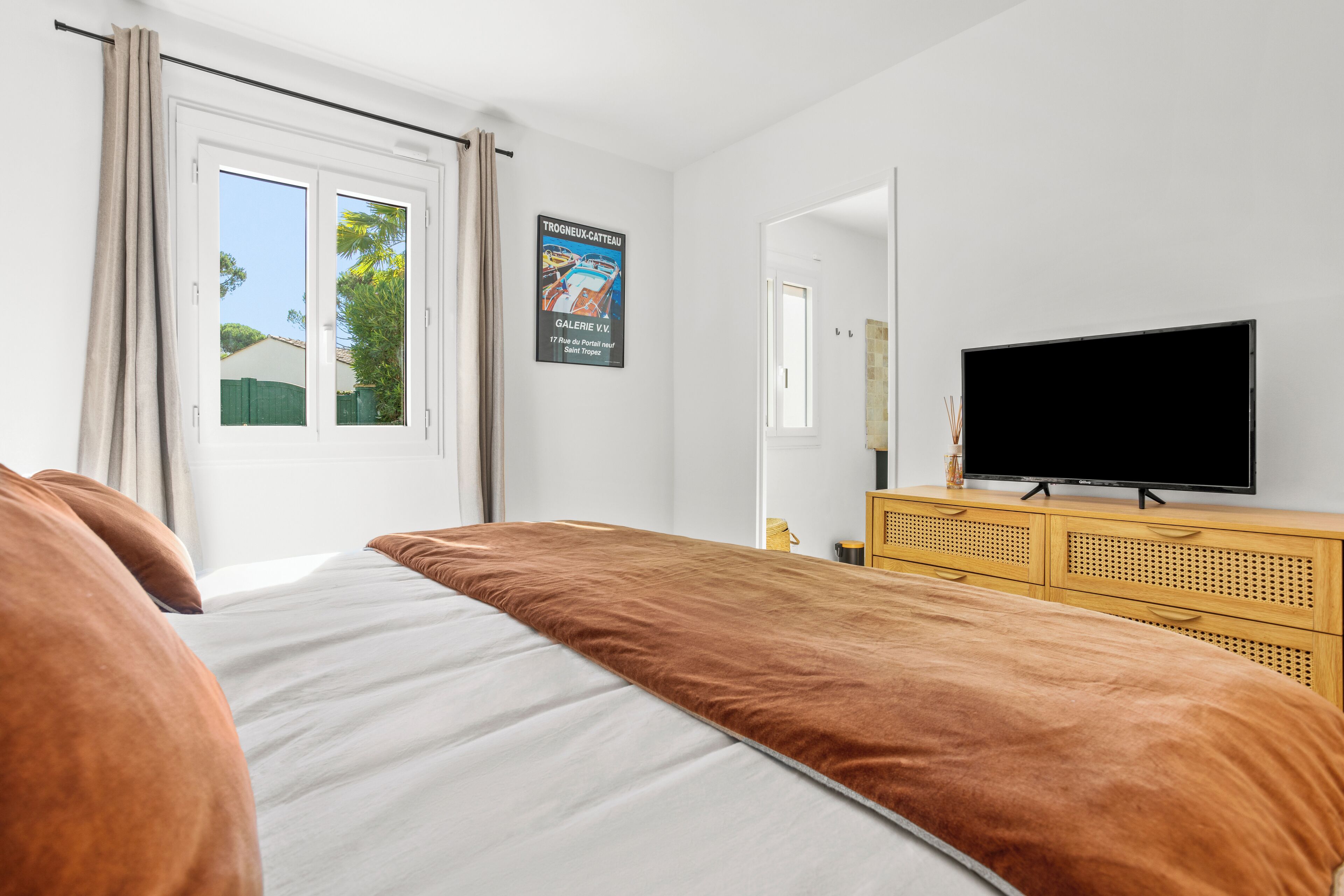 A bedroom with a bed, a television, a wooden dresser, and a poster on the wall.