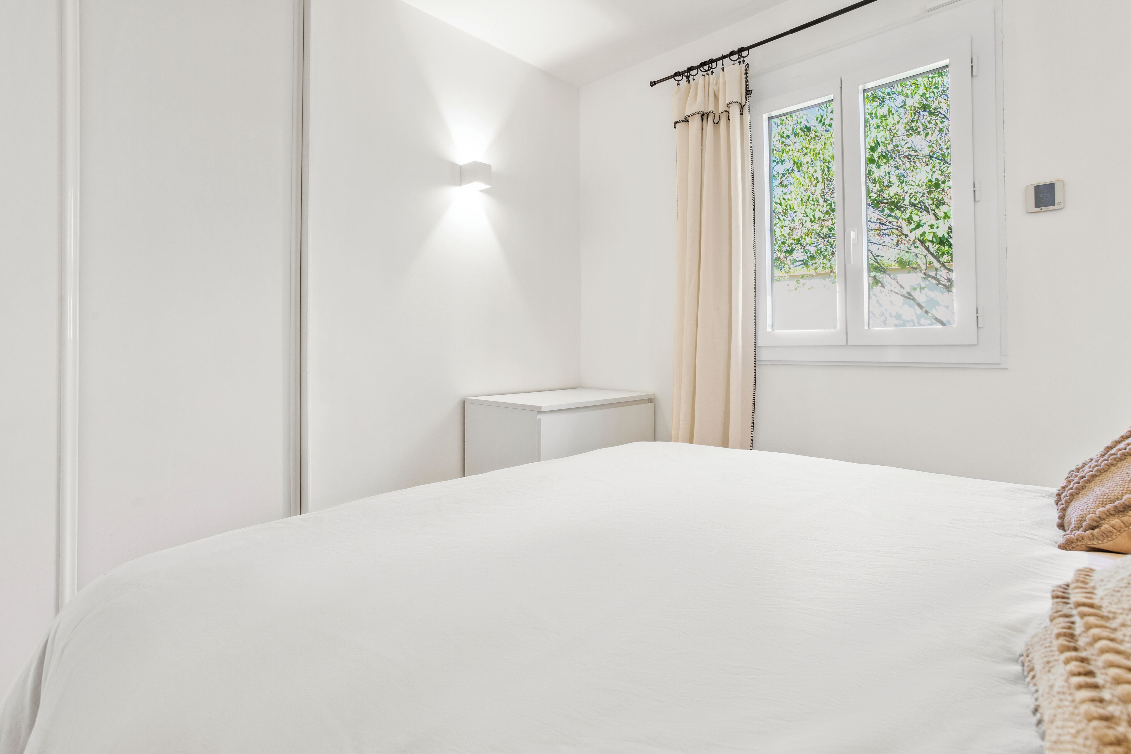 A minimalist bedroom with a large bed, a bedside table, and a window with curtains.