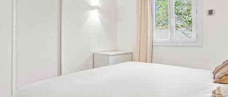 A minimalist bedroom with a large bed, a bedside table, and a window with curtains.