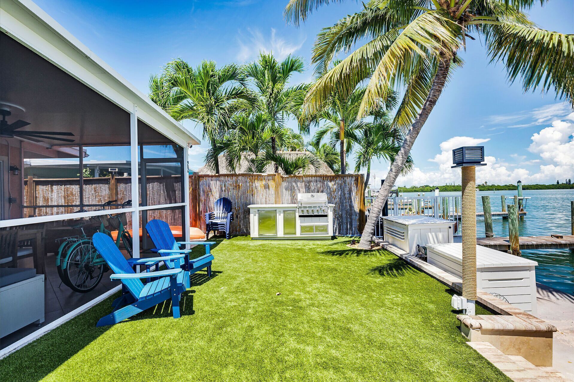 A backyard with a grill, blue chairs, and a view of the water.