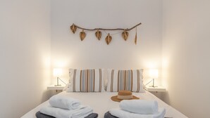 Una cama bien hecha con almohadas a rayas, dos lámparas de noche y una rama con hojas colgando arriba.