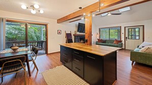 A modern kitchen with a wooden island, a dining area with a table and chairs, a green sofa, and a fireplace.