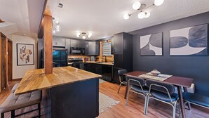 A modern kitchen with dark cabinetry, a wooden island, and a dining area with a table and chairs.